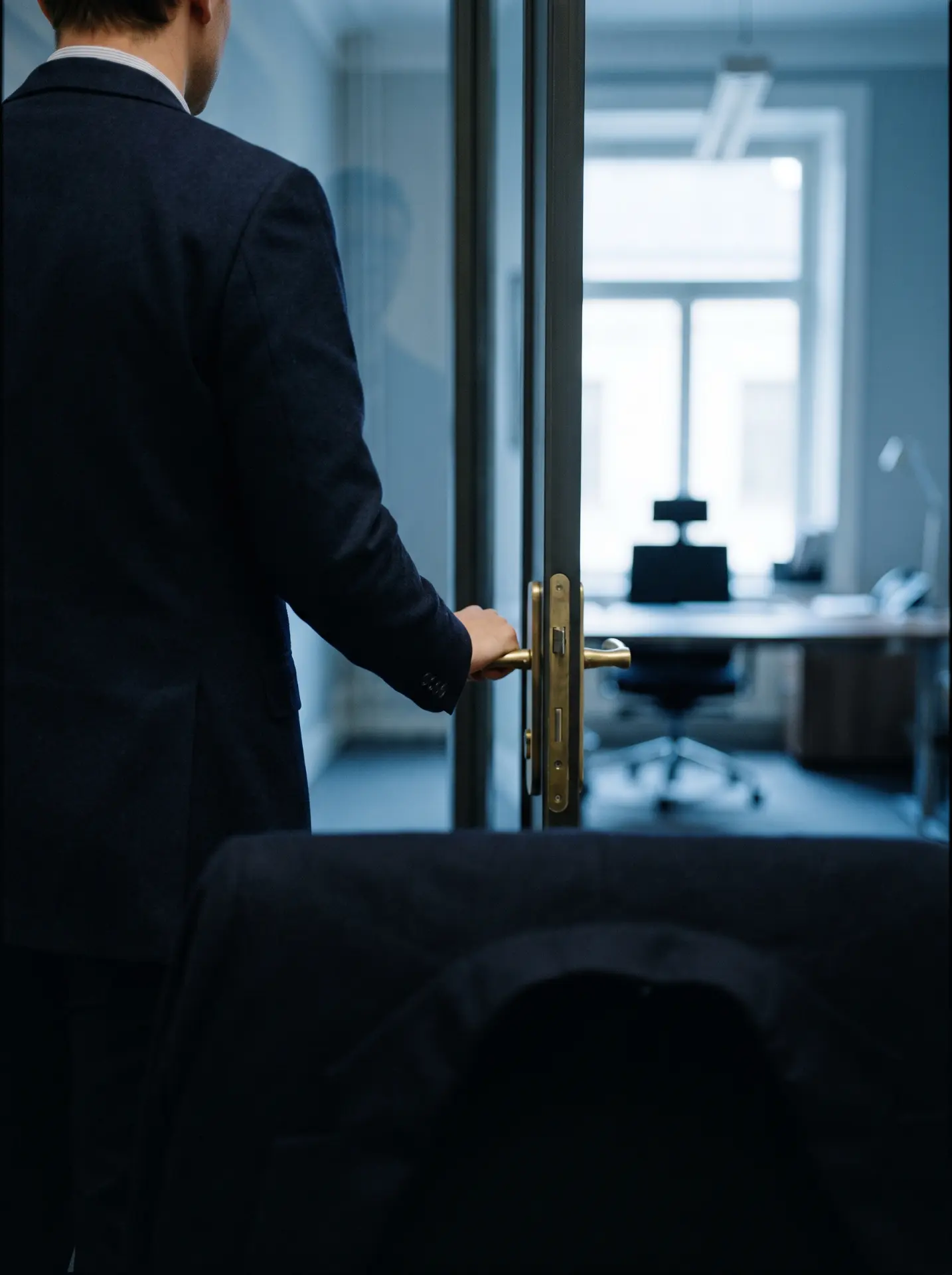 Businessman in a suit opening a glass office door with a brass handle
