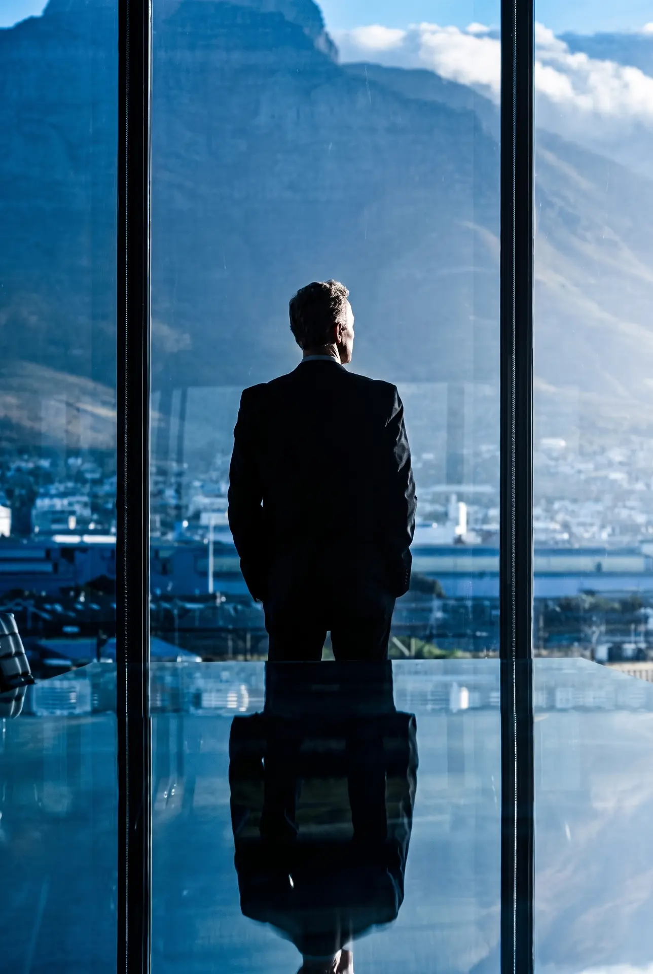 Man in a suit looking out over a mountain view through a glass wall